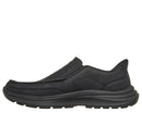 A single black slip-on shoe with a textured leather upper and a thick, cushioned black sole, shown in a side profile view against a plain white background.