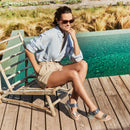 Woman sitting by a pool wearing sunglasses and casual clothing.