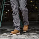 Person wearing brown work boots and gray pants in an industrial setting