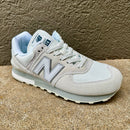 A light gray and white New Balance 574 sneaker with a light blue lining, photographed on a textured concrete surface.