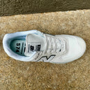 A single New Balance 574 sneaker in white and light gray, photographed from a top-down angle on a textured concrete surface.